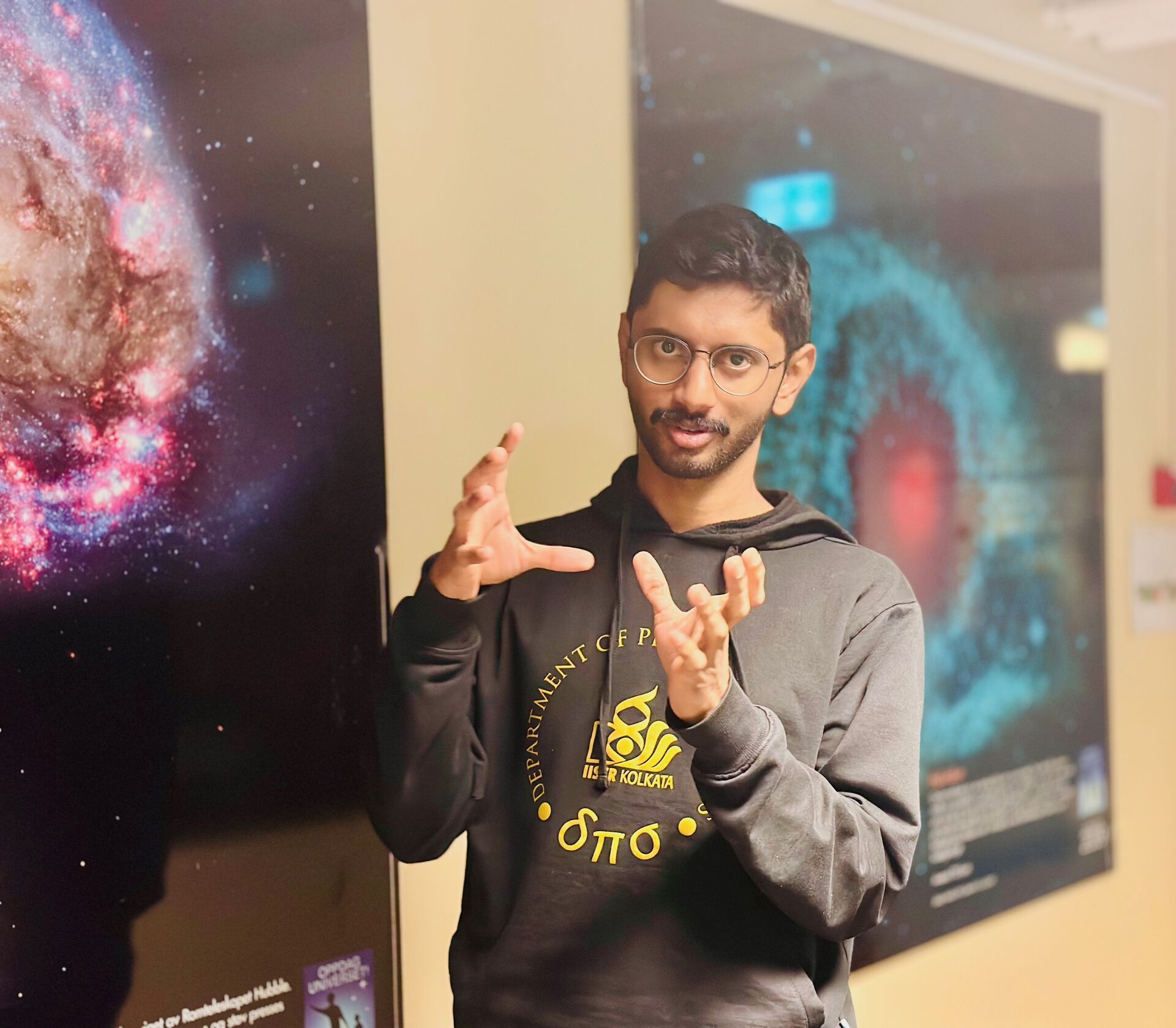 image of a young man with glasses standing in front of images of galaxies