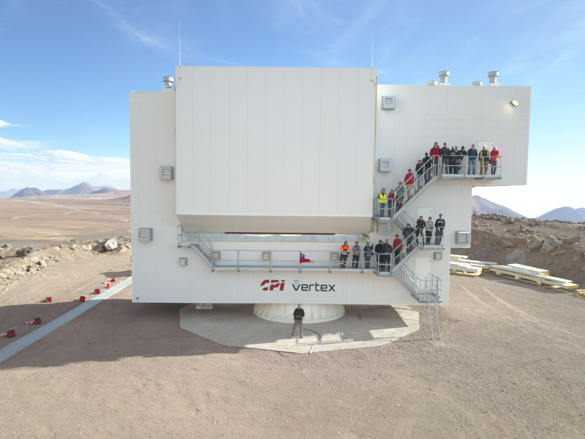 image of a large white structure (the telescope) and people from the observatory posing in front of it