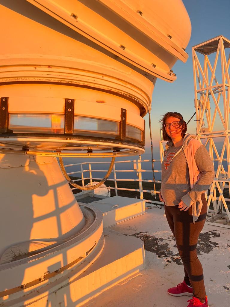 Bildet av en ung smilende kvinne stående ved siden av et teleskop
