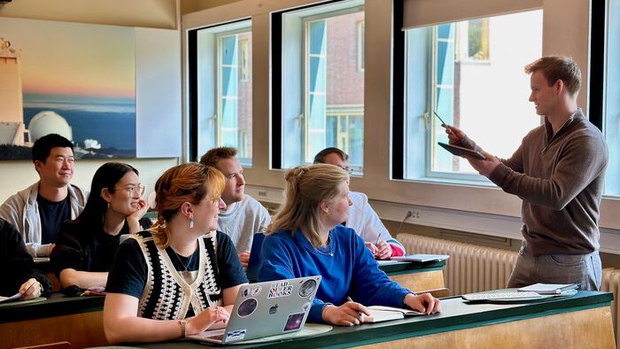 en gruppe av sittende studenter som se og høre på en annen stående student som snakker.