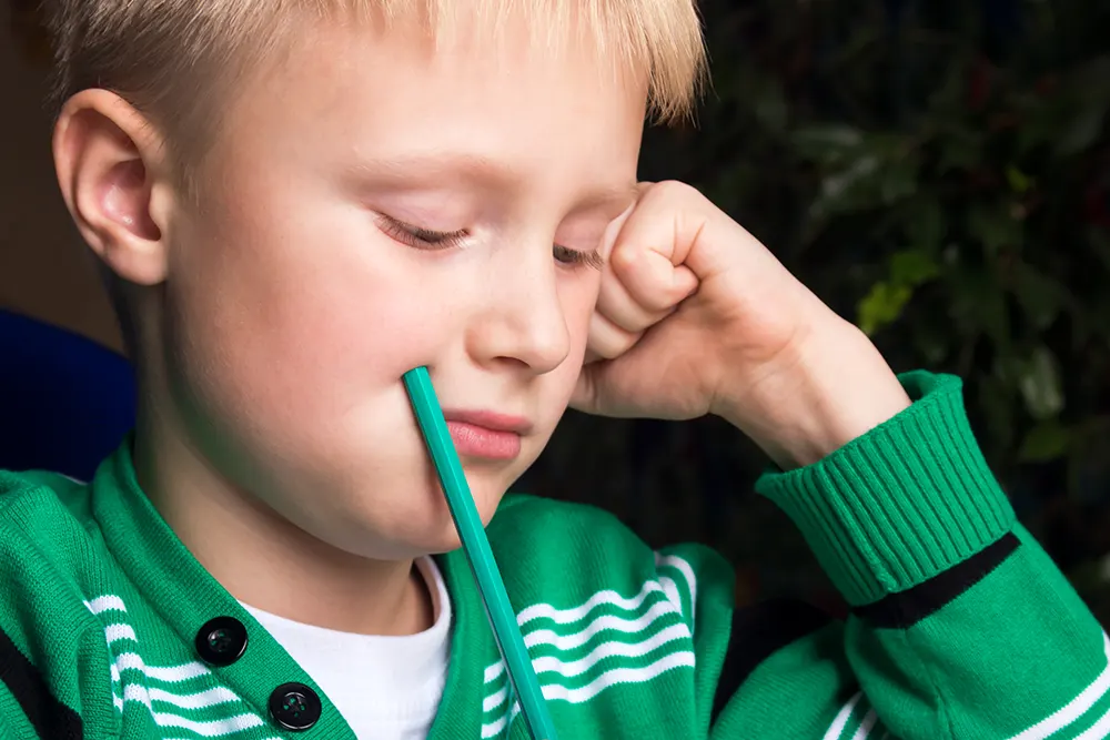 Gut, ca. 10 år, som held ein blyant tli kinnet og funderer på noko