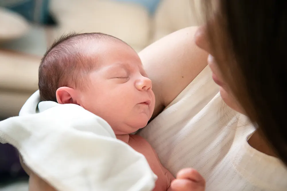 Kvinne som ser ned på babyen ho held i fanget