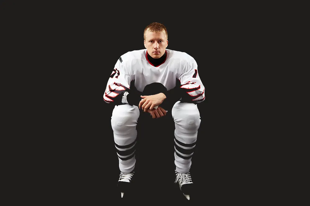 Nedstemt mann i hockeyutstyr som sit mot ein heilt svart bakgrunn