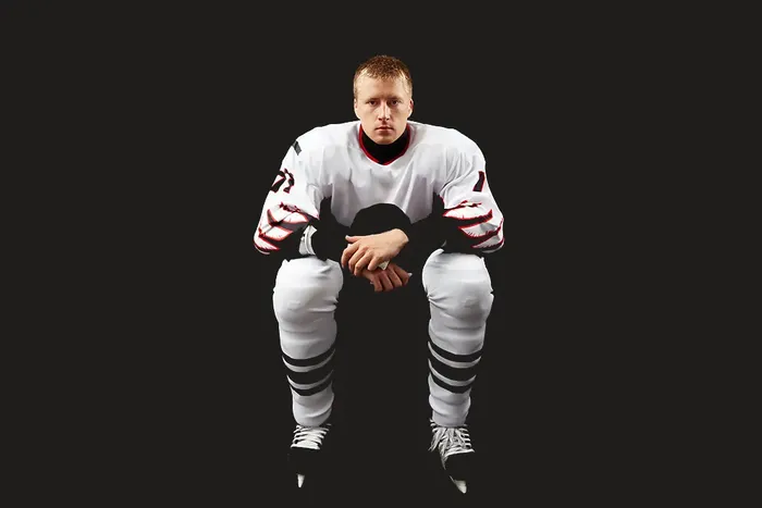 Nedstemt mann i hockeyutstyr som sit mot ein heilt svart bakgrunn