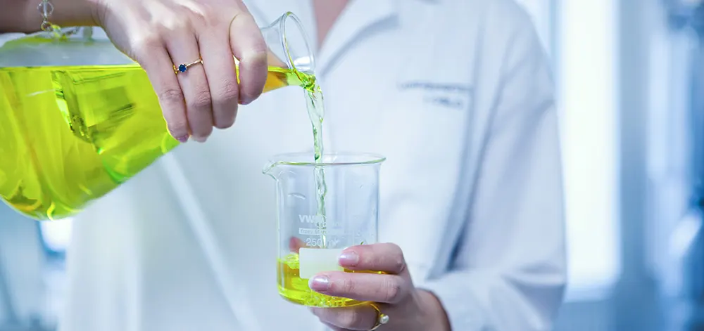 A person pouring a green fluid into a measuring cup