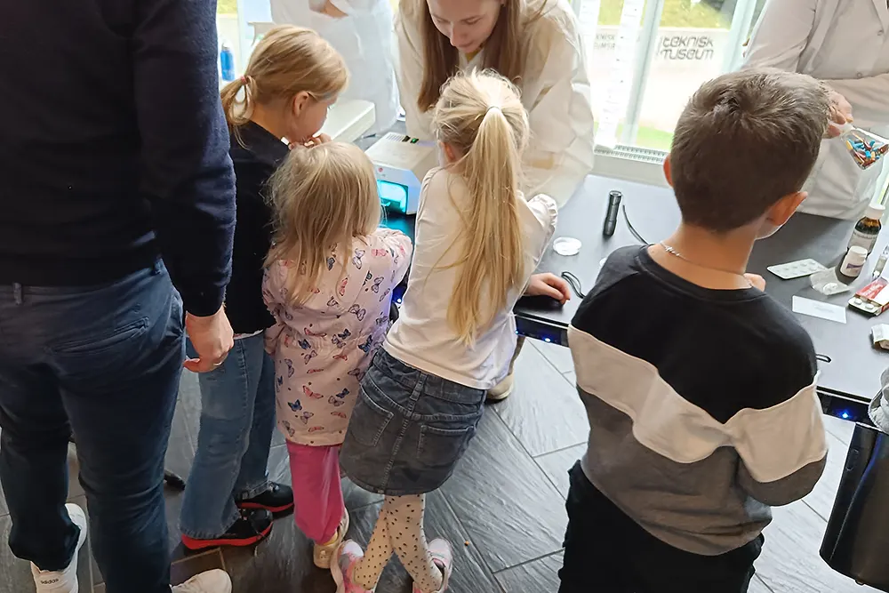 Tre små barn pressar seg mot standbordet