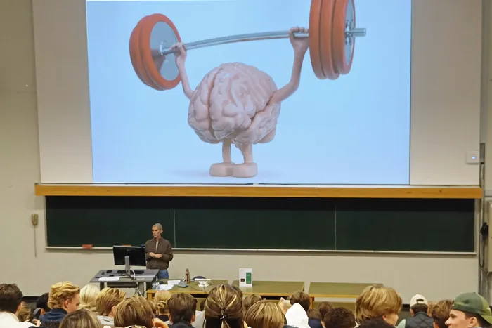 Mona Havik står fremst i auditoriet, med bilete av ein hjerne på lerretet. Vi ser mange bakhovud i salen