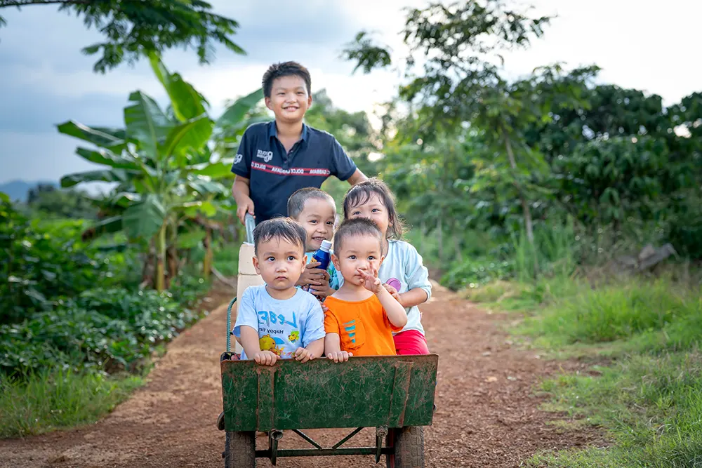 Gutt, ca. 10 år, som triler fire mindre barn i en kjerre/trillebår. Fra Vietnam