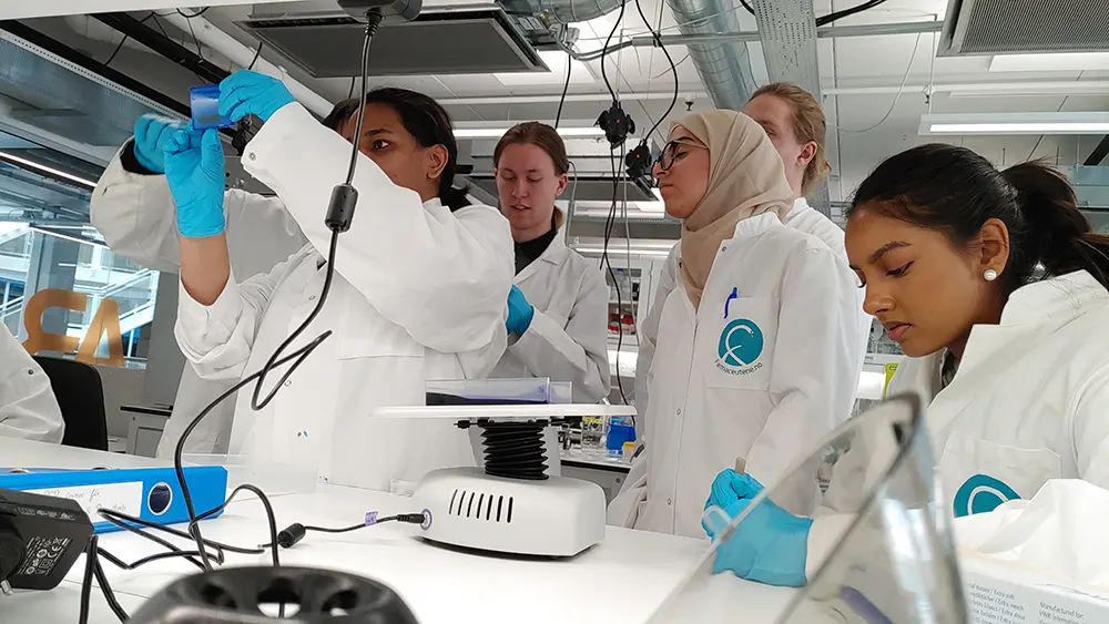Ei gruppe studentar rundt ein undervisar i laboratoriet
