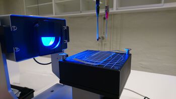 A drop hangs from the tip of a needle and is illuminated by a blue-light source during a surface tension measurement.
