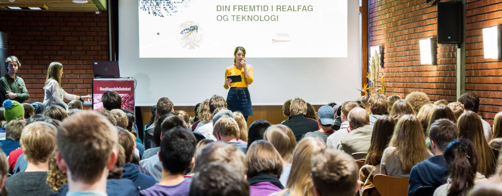 Selda Ekiz står foran mange elever på en scene i Realfagsbiblioteket