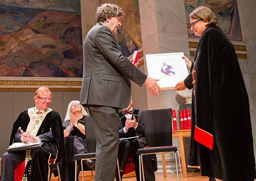 RESEARCH PRIZE: Professor Trond H. Torsvik gets applause from a full-packed audience in the University Aula when he gets the research award from the Deputy Rector Ragnhild H. Hennum. Rector at UiO, Ole Petter Ottesen and the Deputy University Director Tove Kristin Karlsen are seen in the background for the prize winner. Photo: Yngve Vogt, Apollon