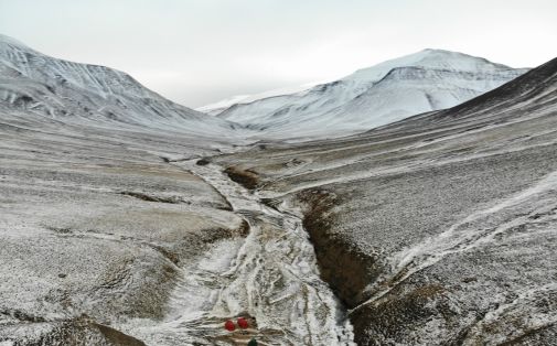 The Permian-Triassic boundary is outcropping in the stream bed of Deltadalen, Svalbard. A 100-meter-long core was drilled one kilometer south of the outcrop in 2014, recovering the boundary interval. The Grusryggen mountain in the background. View to the south. (Photo: Julian Janocha.