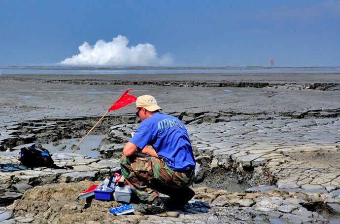 Adriano Mazzini sampling fluid at the Lusi mud eruption, Indonesia. A geysering phase at the crater site is visible in the background.