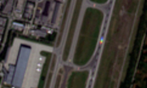 Gardemoen: Satellittbilde av en flyplass.   Satellitten skanner ulike farger etter hverandre, rad for rad. Dette medfører at flyet til høyre som beveger seg en gjengitt i flere farger. FOTO: Sentinel-2A, Copernicus, ESA/Andreas Kääb, Universitetet i Oslo