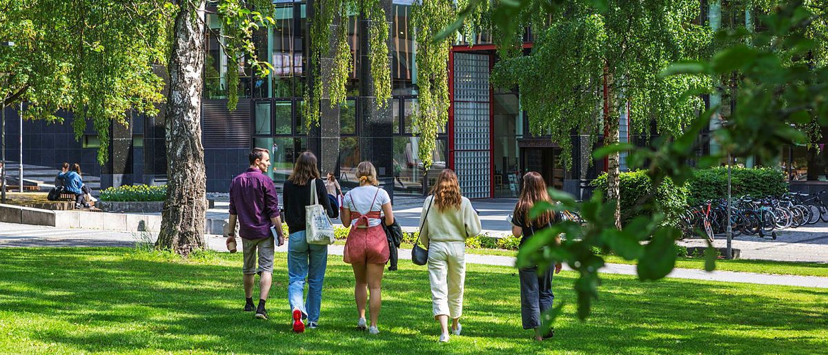 Photo: Students walking side by side over green grass towards the university library. Photo: Jarli og Jordan/UiO
