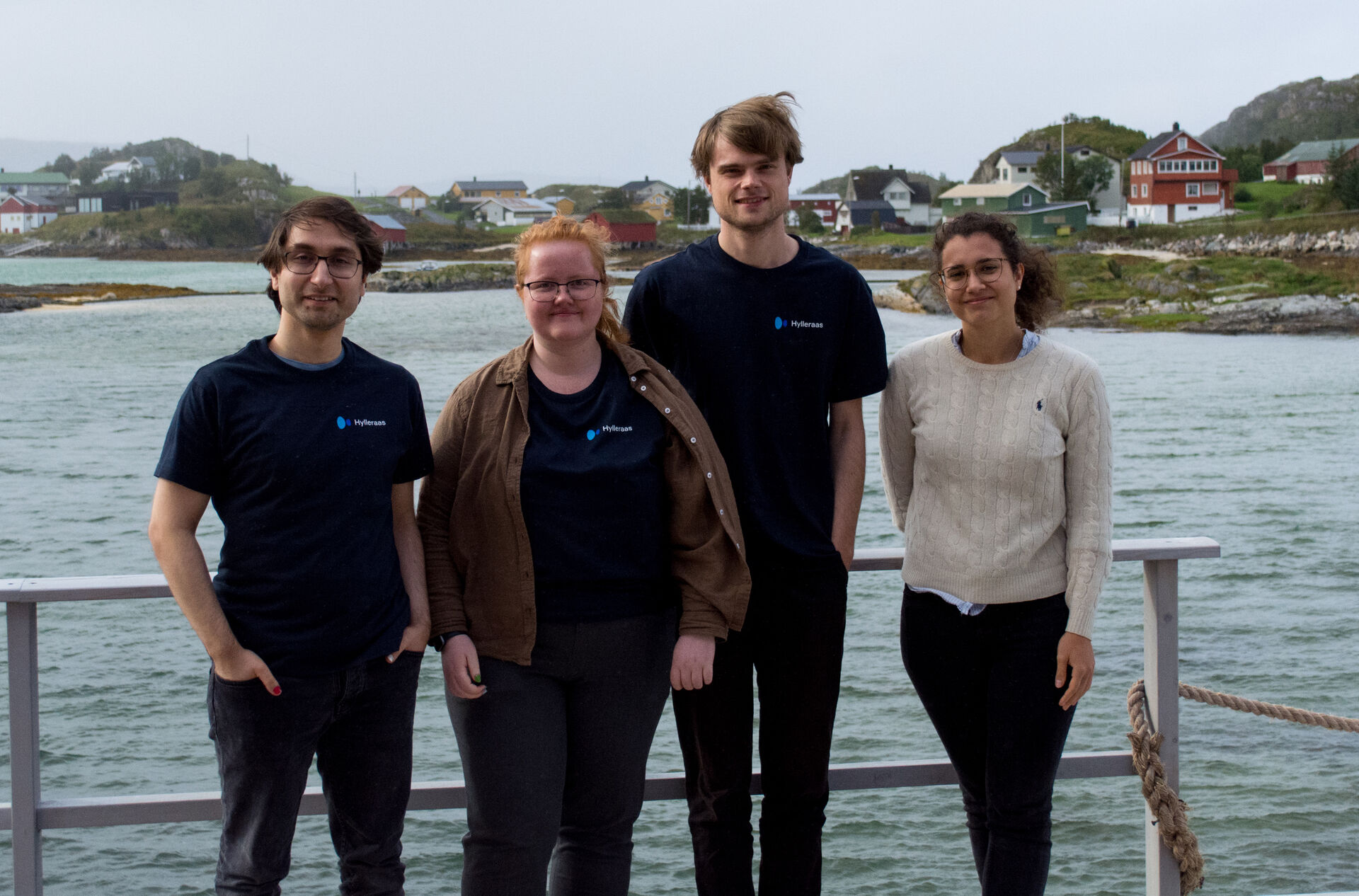 Four young researchers, two man and two ladies, standing with a smile on a bridge with a fjord in behind. 