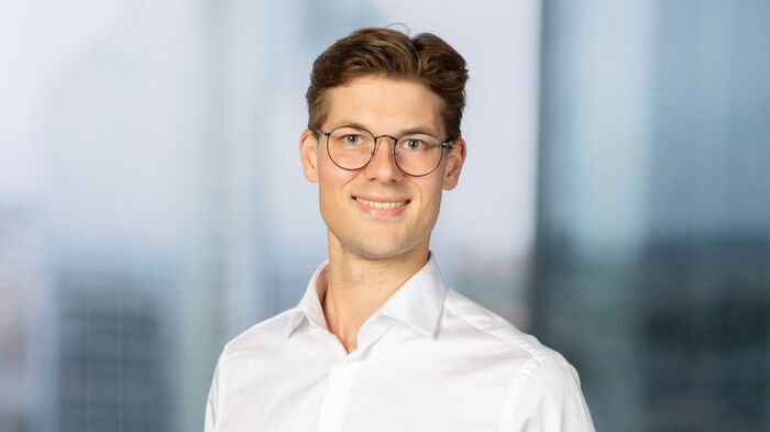 Young man whith a blue shirt and glasses, standing outside and being surrounded by threes in summertime. 