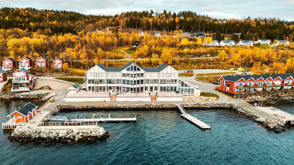 Photo of a white hotel close to a habour. Trees in autumn colored leaves. 