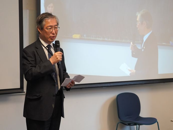 The Deputy Head of Mission at Embassy of Japan (Hajime Matsumura) is holding a short speech in a white seminar room.