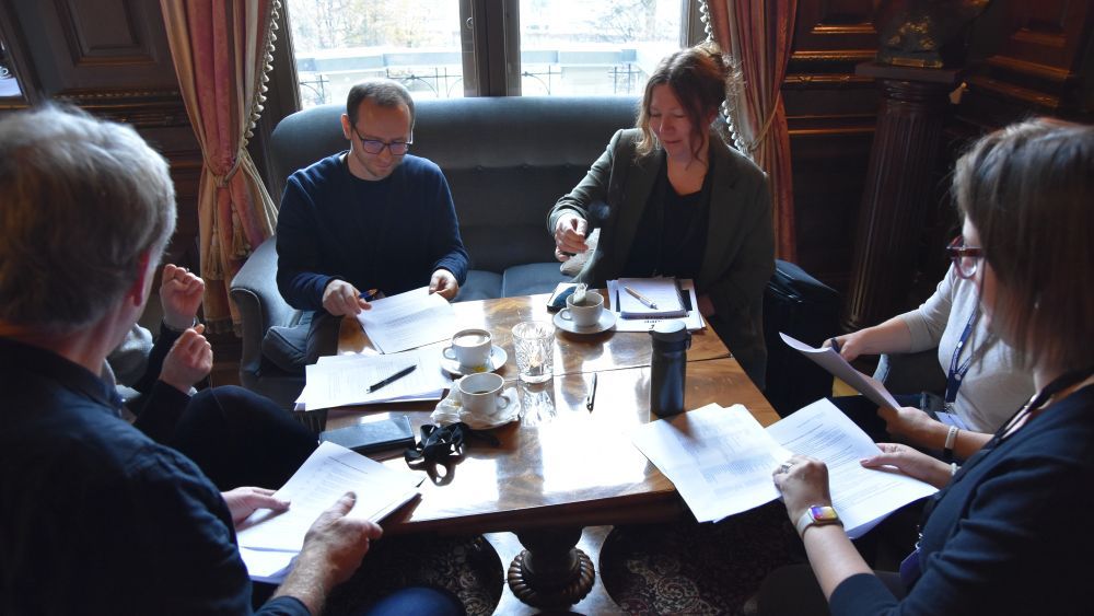 Six scientist sitting around a table, drinking coffe and tea and discussing different matters. 