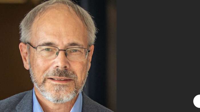 Portrait photo of Trygve Helgaker. He his wearing a blue shirt and grey jacket and is wearing glasses. 
