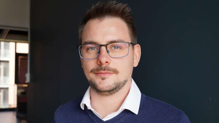 New Postdoc Researcher: Jordan Rio. Young man with glasses and short dark hair, and blue sweather.