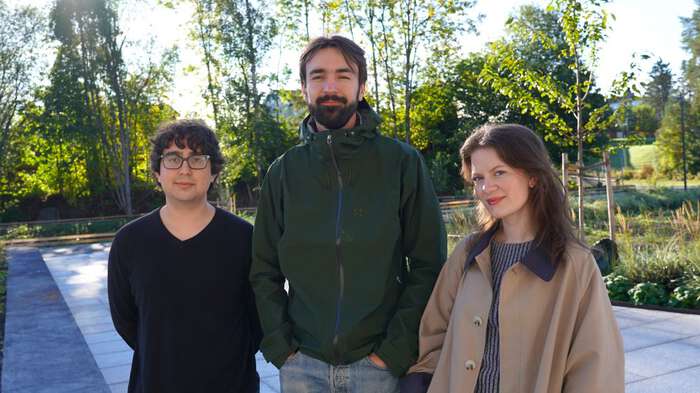 Three young students standing outside at campus outside the Life Science Building with green trees in the background. 