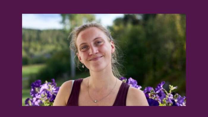 Young woman smiling with purple flowers behind her. 