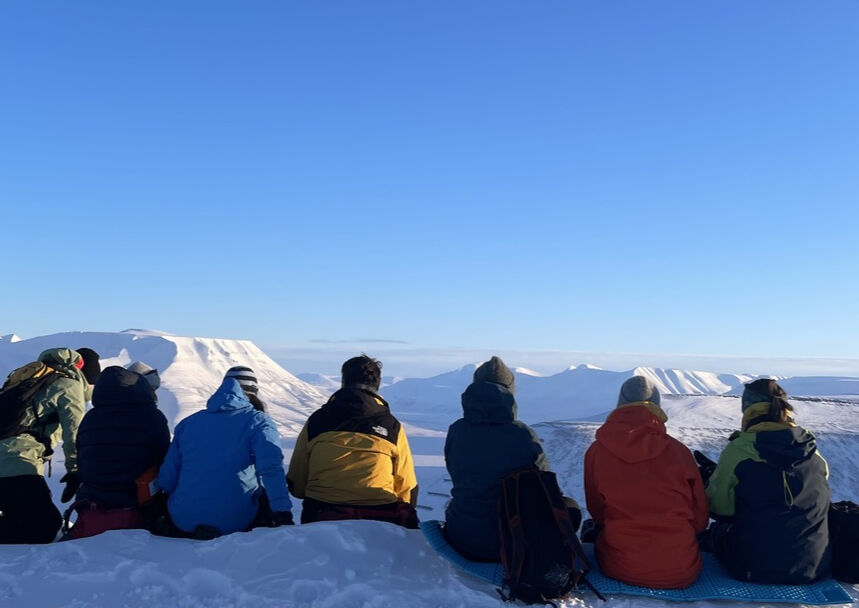 Syv personer som ser ut over snødekt landskap, sett bakfra.