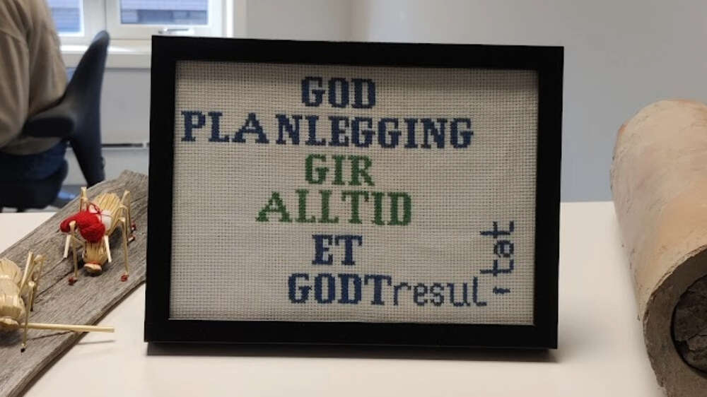 Bilde av broderi med teksten: "God planlegging gir alltid et godt resultat", men hvor teksten ikke får plass innenfor rammen.