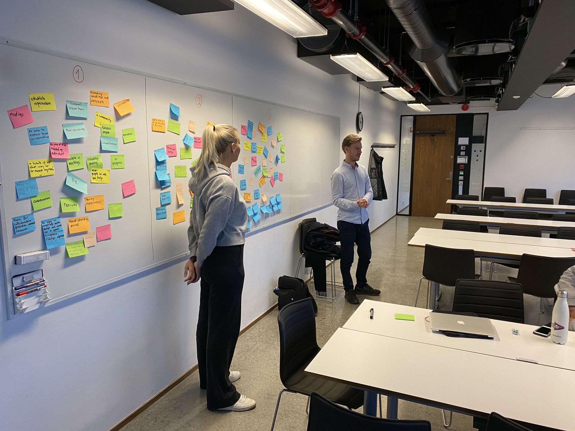 two people discussing post-it notes on a whiteboard