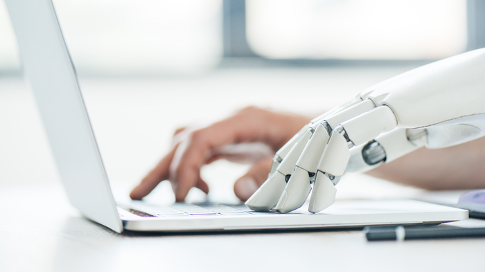 Human and robot hand typing on a laptop