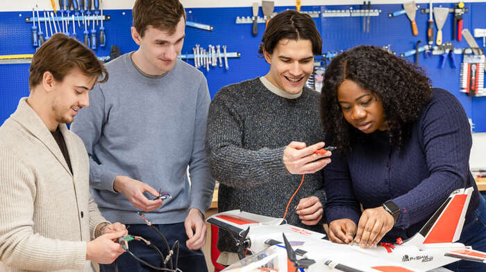 Bilder viser fire studenter i et laboratorie som jobber med en drone