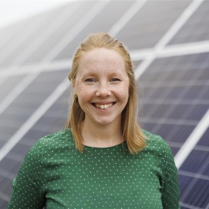 Portrati photo of Torunn Kjeldstad. She is with blond hair and green sweether, standing in front of the solar panel. 