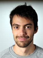 Image may contain: A man (Mateu) is looking straight at the camera and smiling. He is wearing a grey sweater, standing against a grey background.