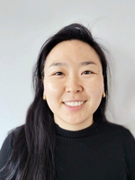 Image may contain: A woman (Tamjidmaa) is looking straight at the camera and smiling. She is wearing a black sweater. She is standing against a grey background. 