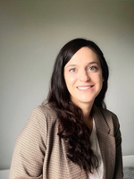 Image may contain: A person (Irene) is smiling and looking straight at the camera. They have long black hair and are wearing a bright brown blazer.