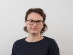 Image may contain: A person  (Liudmila) is looking straight at the camera and smiling. They are wearing a black sweater and glasses, standing against a white background.