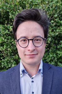 Image may contain: A person (Vladimir) looking straight at the camera. They have short black hair and are wearing a blue shirt and blue blazer.