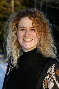 Image may contain: A person (Inga) looking straight at the camera. They have shoulderlength curly brown and blond hair and are wearing a black hoodie and a beige and brown cardigan.