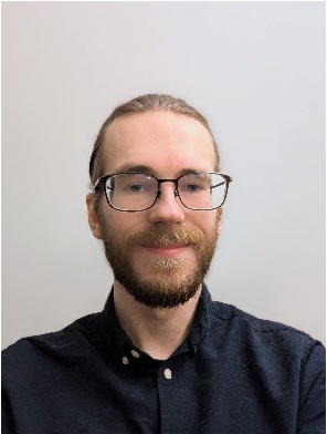 Image may contain: A person (Erlend) is smiling and looking straight at the camera. They have brown hair and are wearing a dark blue shirt.
