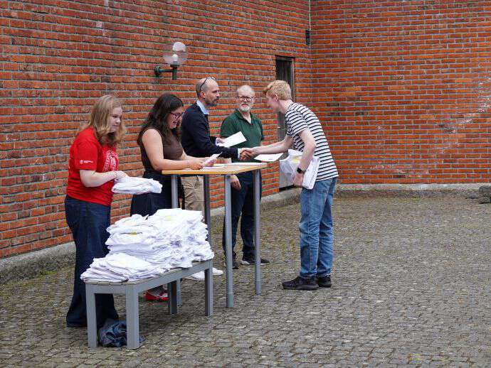 Mann i blå genser gir et dokument, borgerbrev, til en ung mannlig student. 