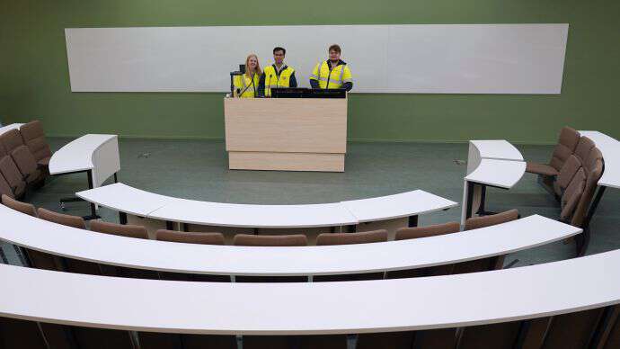 Tre studenter står bak kateter og ser ut over et auditorium.