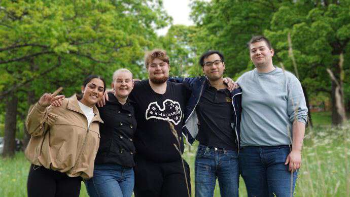 Fem glade studenter, to jenter og tre gutter står ute på en gresseng ved campus.