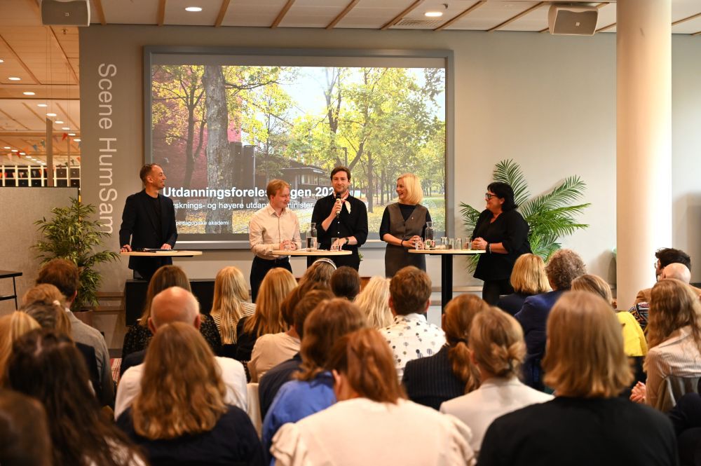 gruppe mennesker i sal hører på fire mennesker i paneldebatt
