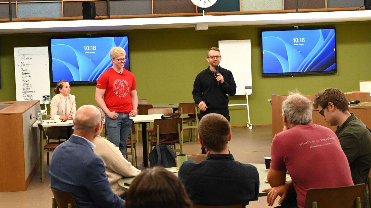 student og mann snakker foran gruppe mennesker
