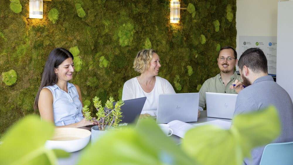 gruppe mennesker sitter rundt et bord med PC'er, snakker og jobber