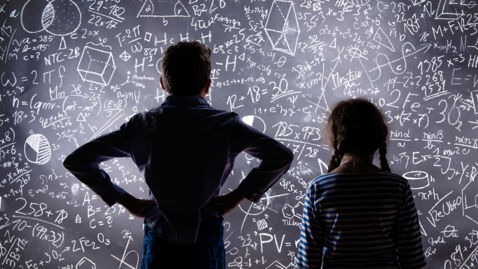 En gutt og ei jente som ser på tavle med formler og uttrykk fra naturvitenskap og matematikk.