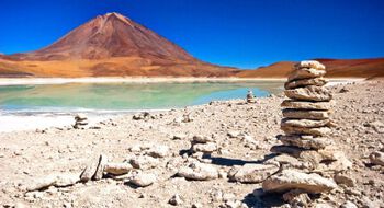 A stack of stones by a lake and a red mountain.
